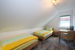 Ein kleiner, gut beleuchteter Raum mit zwei Einzelbetten, einem Schreibtisch mit Stuhl und einem Fenster mit Blick auf einen Zaun.