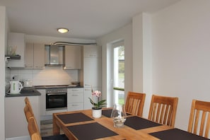 Eine moderne Küche mit weißen Schränken, einem eingebauten Backofen und einem Essbereich mit einem Holztisch und Stühlen.