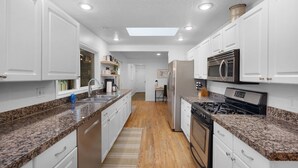 Una cocina moderna con armarios blancos, encimeras de granito, electrodomésticos de acero inoxidable y un tragaluz.
