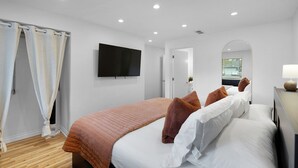 Una habitación de hotel moderna con una cama grande, un televisor de pantalla plana en la pared y un baño visible a través de un arco.