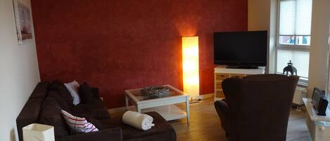 A living room with a brown sofa, a white coffee table, a TV, and a window with blinds.
