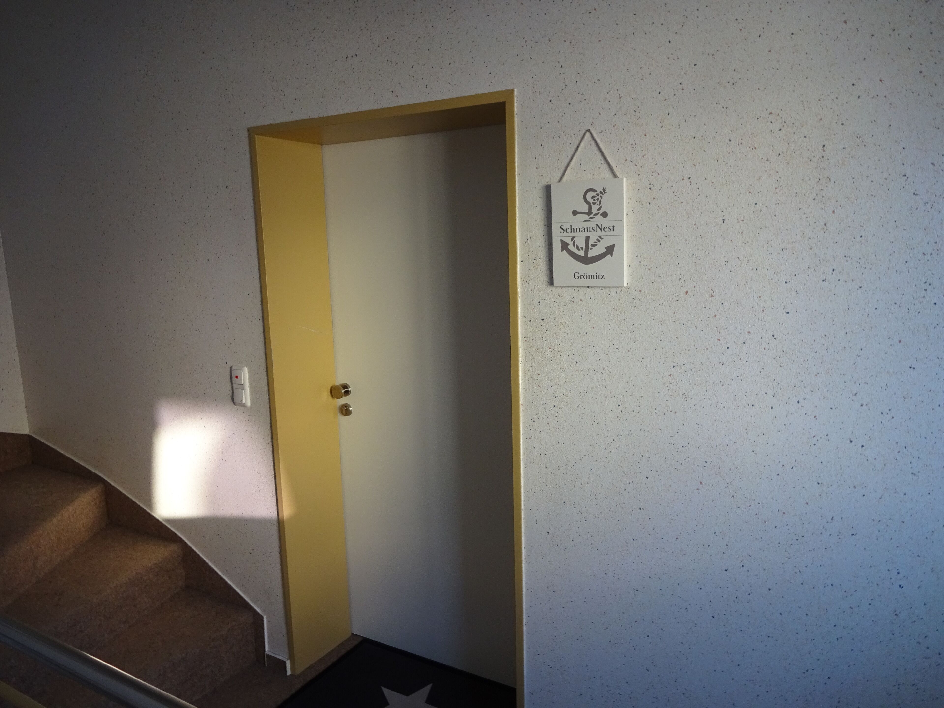 Ein Flur mit einer geschlossenen Tür, einer Treppe und einem an der Wand befestigten Schild mit einem Logo und Text.