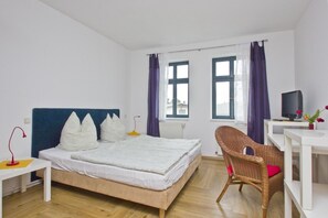 A bedroom with a bed, a desk, a chair, a TV, and a window with curtains. - F-1065 Brunnenaue - Brunnenaue Group Home F-1065 (Sagard)