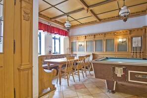 Una sala de billar con muebles de madera, una mesa de billar y una ventana con cortinas rojas.