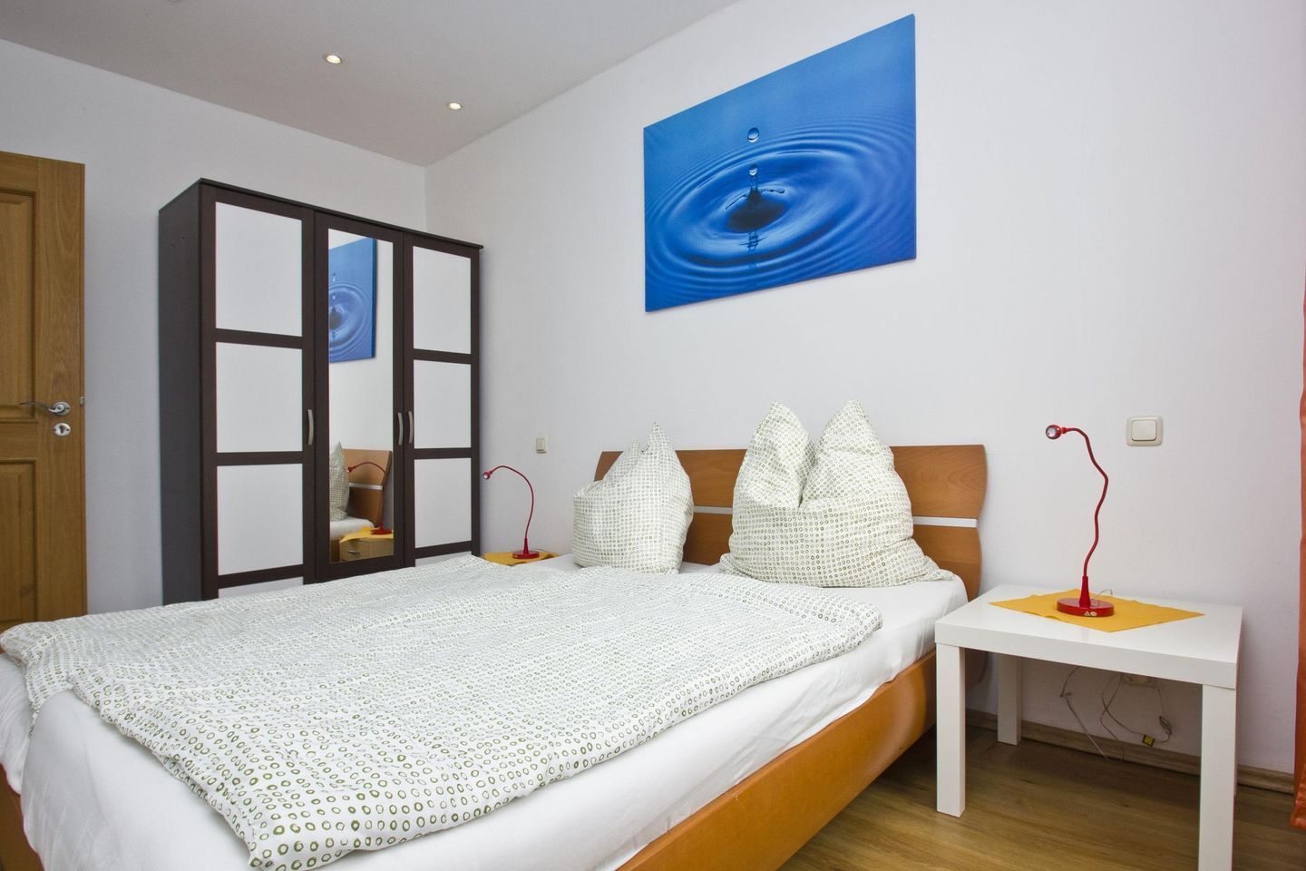 A bedroom with a bed, a nightstand, a wardrobe, and a wall-mounted painting.
