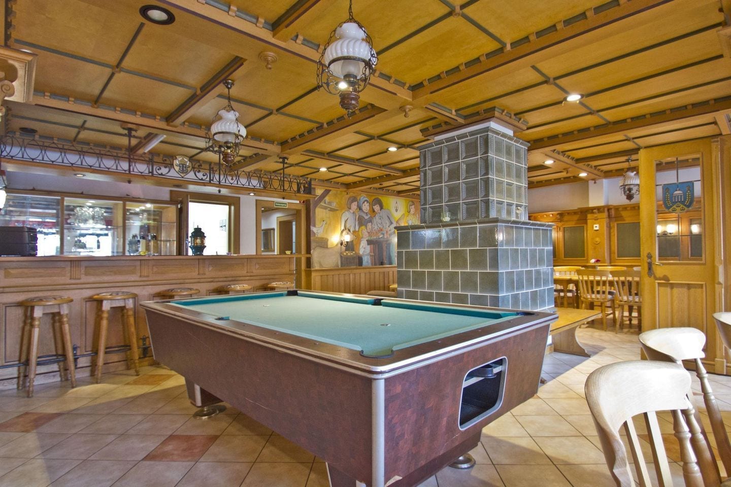 A pool table in a room with wooden ceiling beams, a bar area, and a mural on the wall.