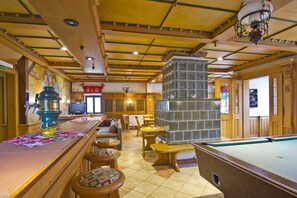 Zona de bar con mesa de billar, taburetes, máquina de café y chimenea.