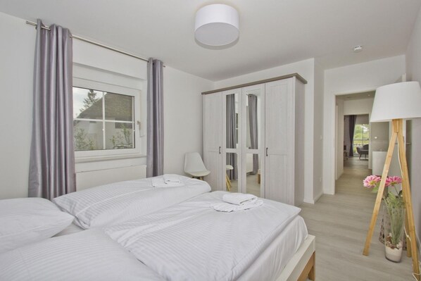 A bedroom with two beds, a wardrobe, a lamp, and a potted plant.
