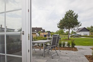 A patio with a table and chairs, a tree, and a car in the background.