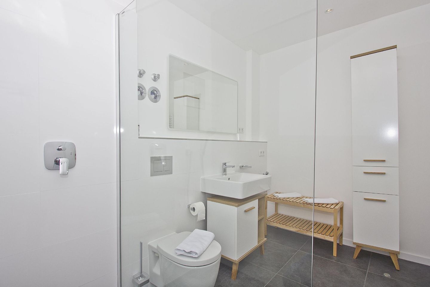 Un baño moderno con mampara de vidrio, lavabo blanco, inodoro y banco de madera.