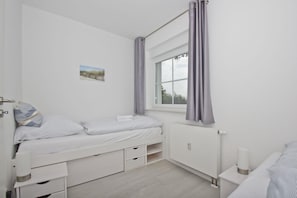 Una habitación pequeña y limpia con una cama individual, una mesita y una ventana con cortinas.