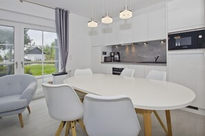 Une cuisine moderne avec des meubles blancs, un four à micro-ondes de la marque Bosch et une grande table à manger avec quatre chaises.