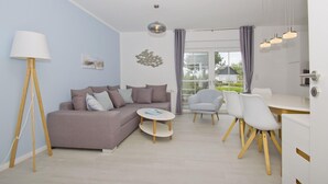 A modern living room with a grey sofa, a round coffee table, and a dining area with a white table and chairs. - Modern vacation apartment with private terrace - Haus Inselwind FeWo MEERglück - (Gager)