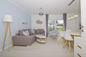 Una sala de estar moderna con un sofá gris, una mesa redonda de centro y un comedor con una mesa blanca y sillas.