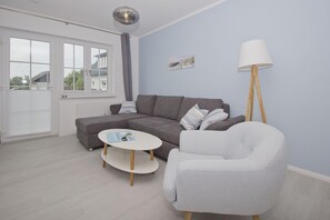 Un salon moderne avec un canapé d’angle gris, une table basse ronde blanche et un fauteuil gris.