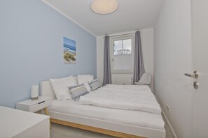A bedroom with a bed, bedside table, lamp, and a window with curtains. - Modern vacation apartment with private terrace - Haus Inselwind FeWo MEERsand - House (Gager)
