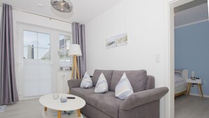 A modern living room with a grey sofa, a round table, and a lamp. - Free use of the AHOI adventure pool and sauna - Haus Inselwind FeWo MEERbodden - (Gager)