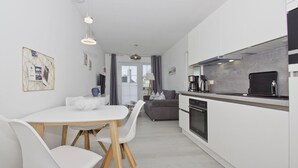 A modern kitchen with a built-in oven and a dining area with a white table and chairs. - Free use of the AHOI adventure pool and sauna - Haus Inselwind FeWo MEERbodden - (Gager)