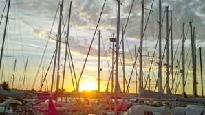Una marina con diverse barche a vela ormeggiate, con alberi e sartiame visibili, sotto un cielo al tramonto.