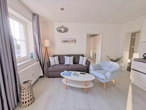 Un salon moderne avec un canapé gris, un fauteuil bleu clair, une table basse blanche et un lampadaire.