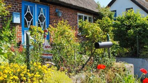 Una casa tradizionale con tetto di paglia e una porta blu, immersa in un giardino ricco di piante e fiori.