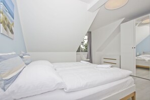 A modern bedroom with a large bed, a bedside table, a chair, and a wardrobe. - Modern vacation apartment with garden - Haus Inselwind FeWo MEERbucht - House (Gager)