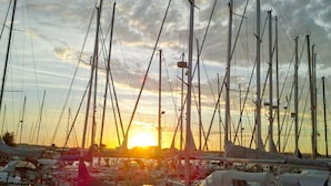 Un puerto deportivo con varios veleros amarrados, destacando sus mástiles y aparejos, bajo un cielo al atardecer.