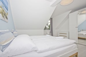 A modern bedroom with a large bed, a bedside table, a chair, and a wardrobe. - Modern vacation apartment with a garden - Inselwind House FeWo MEERbucht - House (Gager)
