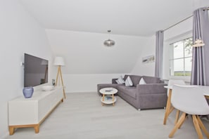A modern living room with a grey sofa, white TV stand, and a small round table. - Modern vacation apartment with a garden - Inselwind House FeWo MEERbucht - House (Gager)