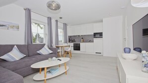 Una sala moderna con un sofá gris, una mesita redonda y una cocina al fondo.