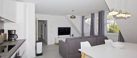 Una sala moderna con un sofá gris, una mesa de comedor blanca y un televisor al fondo.