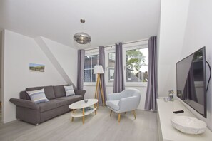 Een moderne woonkamer met een grijze bank, een witte salontafel, een grijze fauteuil en een grote flatscreen-tv.