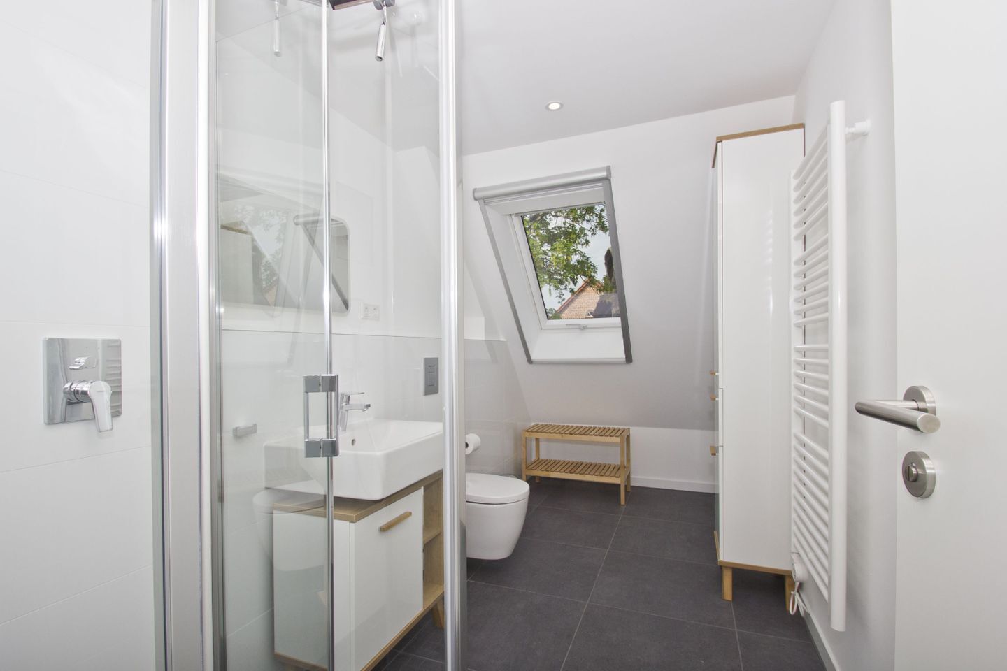 A modern bathroom with a glass shower enclosure, a white sink, a toilet, and a small wooden shelf.