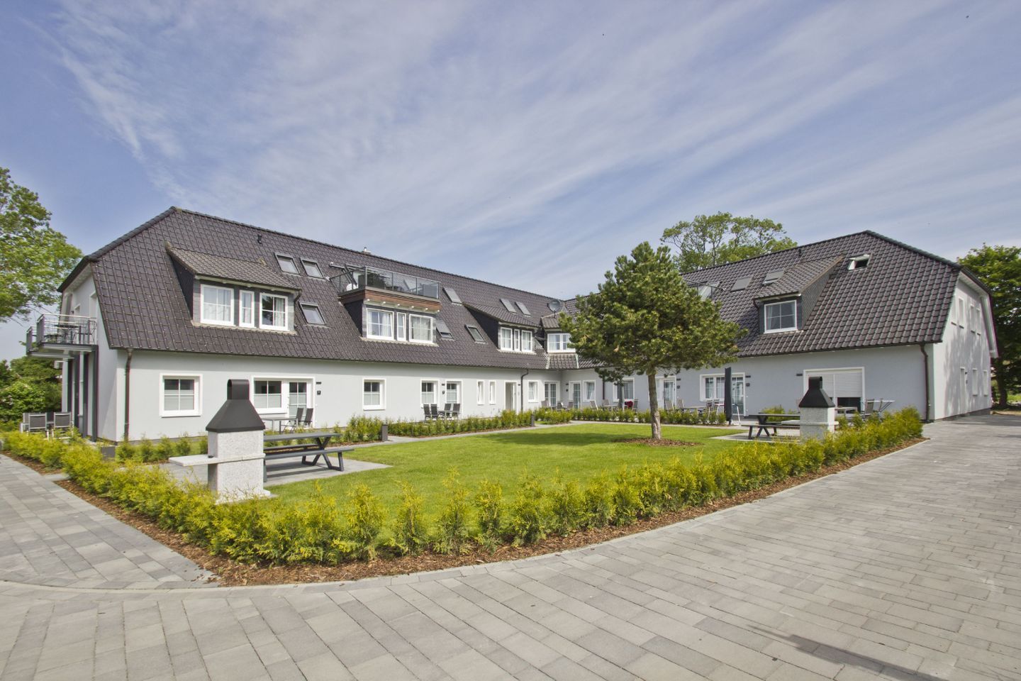 A modern residential building with a courtyard, multiple windows, and a paved walkway.