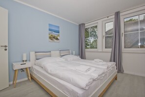 A bedroom with a bed, bedside tables, a window with curtains, and a wall-mounted picture. - Free use of the AHOI adventure pool and sauna - Haus Inselwind FeWo MEERwellen - (Gager)