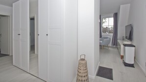 Habitació moderna i ben il·luminada amb un armari gran, una petita zona de seients amb una cadira i una taula, i una televisió sobre un suport.