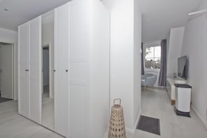 A modern, well-lit room with a large wardrobe, a small seating area with a chair and a table, and a television on a stand. - Free use of the AHOI adventure pool and sauna - Haus Inselwind FeWo MEERwellen - (Gager)