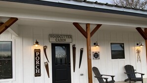 Una cabaña con un porche, un letrero que dice "WOODCUTTER CABIN" y dos sillas Adirondack afuera.