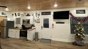 Una cocina con armarios blancos, un refrigerador de acero inoxidable, un microondas y una estufa. Hay un árbol de Navidad y un letrero que dice "Adventure Awaits".