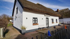 A white cottage with a thatched roof, a wooden bench outside, and a brick pathway leading to the entrance.