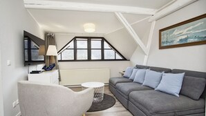 A modern loft-style room with a grey sofa, a white armchair, a small round table, and a TV mounted on the wall.