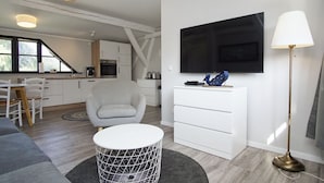 A modern living room with a white sofa, a round coffee table, a grey armchair, a white TV stand, and a floor lamp.