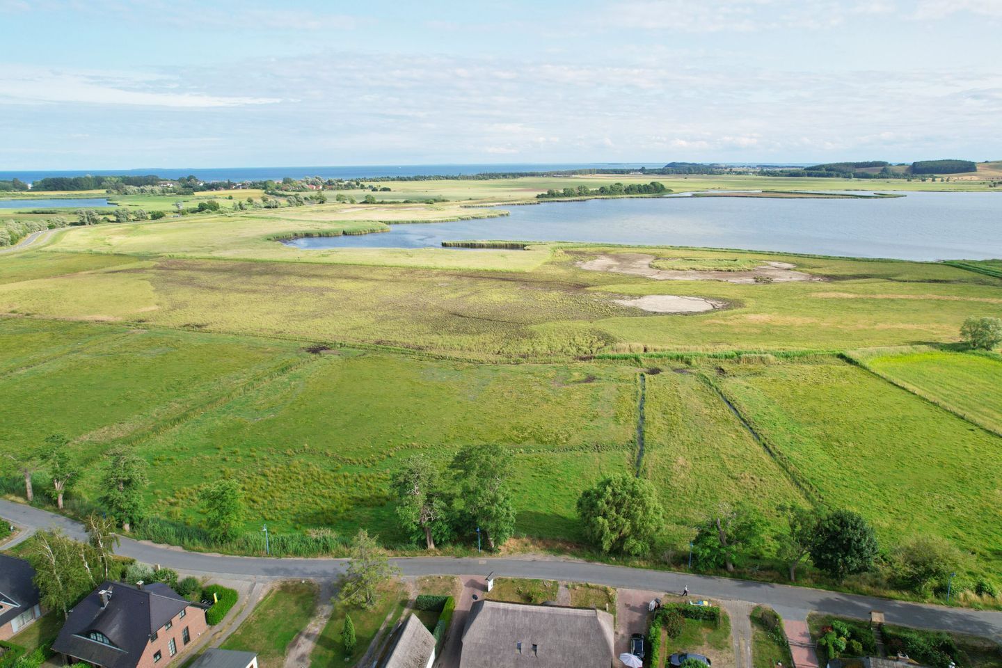 An aerial view of a residential area with houses, a road, and a large body of water.