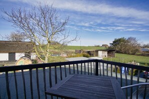 A wooden deck with a metal railing, overlooking a rural landscape with open fields, a few buildings, and a clear sky. - Close to the sea, quiet location, access to the pool and sauna - Haus Büdnerstube FeWo 5 (Middelhagen)