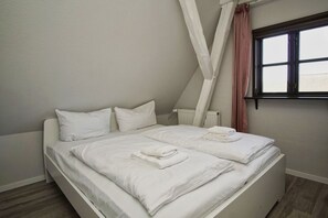A bedroom with a large bed, white bedding, a window with a view, and a white ceiling. - Close to the sea, quiet location, use of swimming pool and sauna - Haus Büdnerstube FeWo 5 (Middelhagen)
