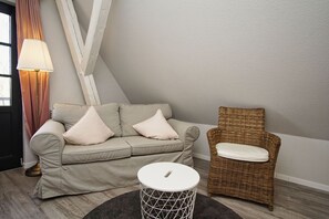 A modern living room with a sofa, a wicker chair, a small round table, and a lamp. - Close to the sea, quiet location, use of swimming pool and sauna - Haus Büdnerstube FeWo 5 (Middelhagen)