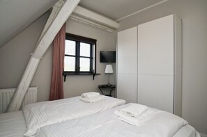 A bedroom with a bed, a window, a TV, and a radiator. - Close to the sea, quiet location, access to the pool and sauna - Haus Büdnerstube FeWo 5 (Middelhagen)