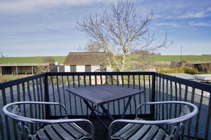 A wooden deck with a table and two chairs, overlooking a rural landscape with a tree and a building in the background. - Close to the sea, quiet location, use of swimming pool and sauna - Haus Büdnerstube FeWo 5 (Middelhagen)