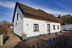 A white cottage with a thatched roof, a wooden bench outside, and a brick pathway leading to the entrance. - Close to the sea, quiet location, use of swimming pool and sauna - Haus Büdnerstube FeWo 2 (Middelhagen)