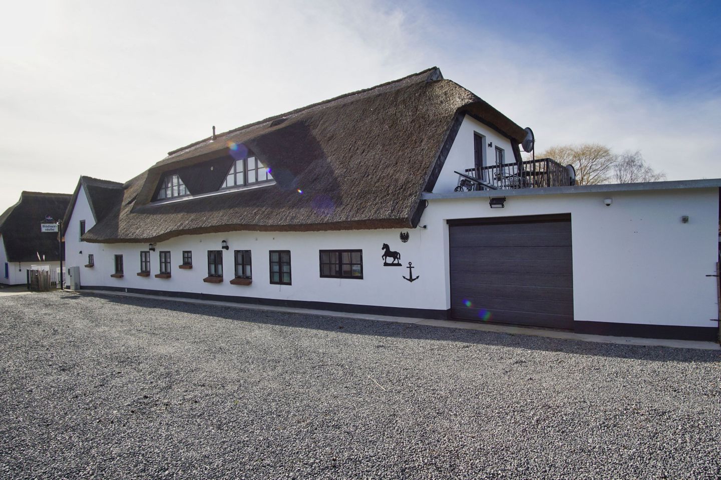 A white building with a thatched roof, multiple windows, and a garage door.